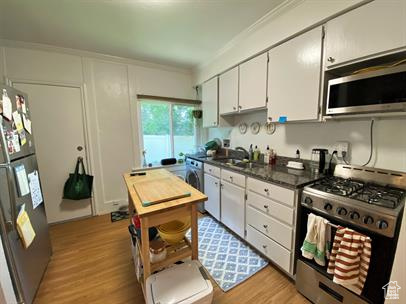 Kitchen with appliances with stainless steel finishes, dark countertops, light wood-style flooring, white cabinetry, and ornamental molding