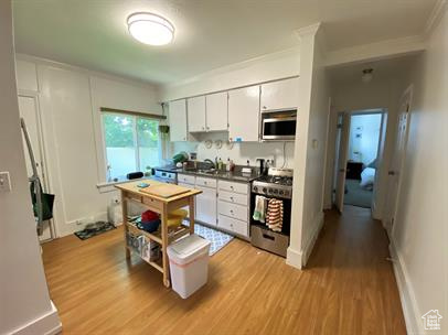 Kitchen featuring appliances with stainless steel finishes, light wood-style floors, dark countertops, white cabinets, and ornamental molding