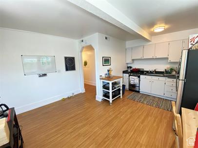 Kitchen featuring stainless steel appliances, arched walkways, white cabinetry, light wood-type flooring, and dark countertops