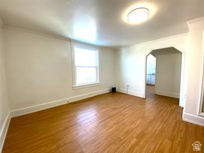 Spare room featuring arched walkways, wood finished floors, and ornamental molding