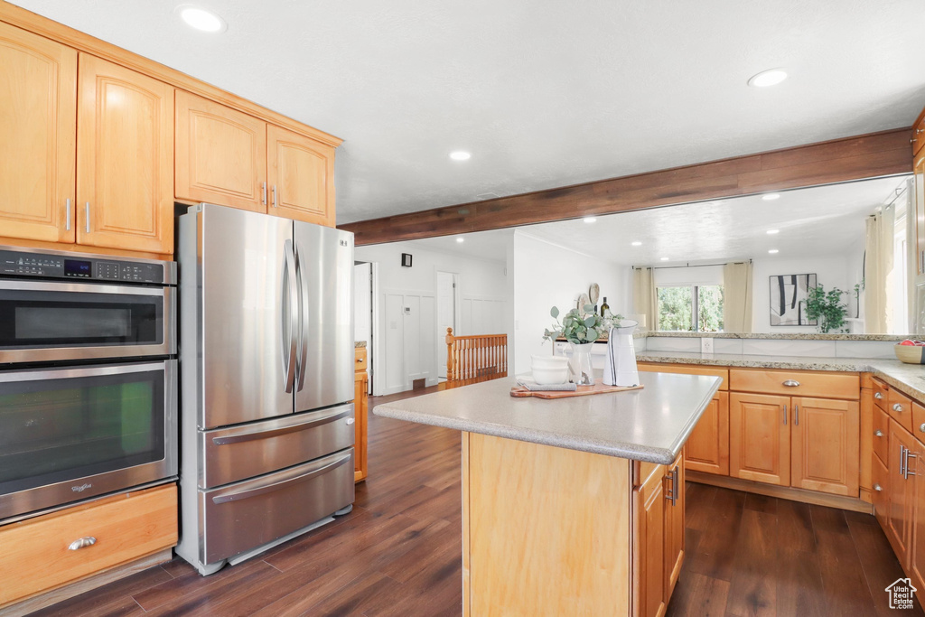 Kitchen featuring stainless steel appliances, beam ceiling, dark wood-style floors, a kitchen island, and light brown cabinetry