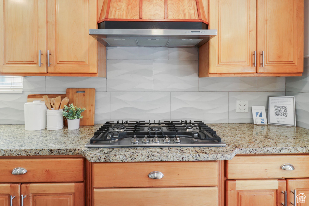 Kitchen featuring stainless steel gas cooktop, decorative backsplash, ventilation hood, and light stone counters