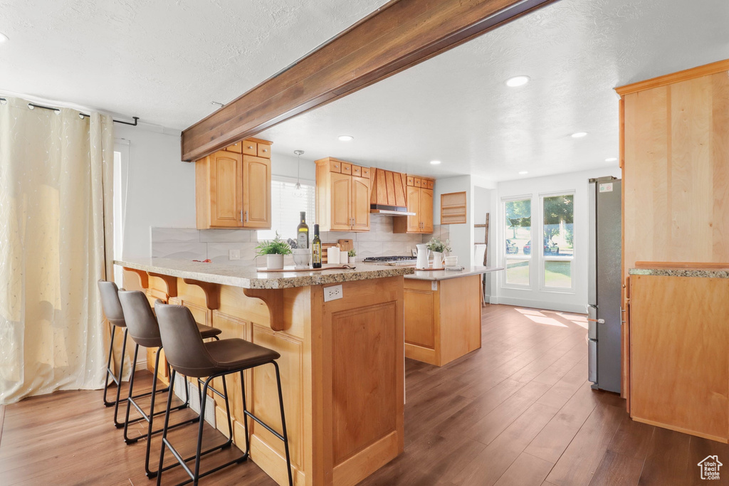 Kitchen with freestanding refrigerator, a peninsula, backsplash, a breakfast bar area, and recessed lighting