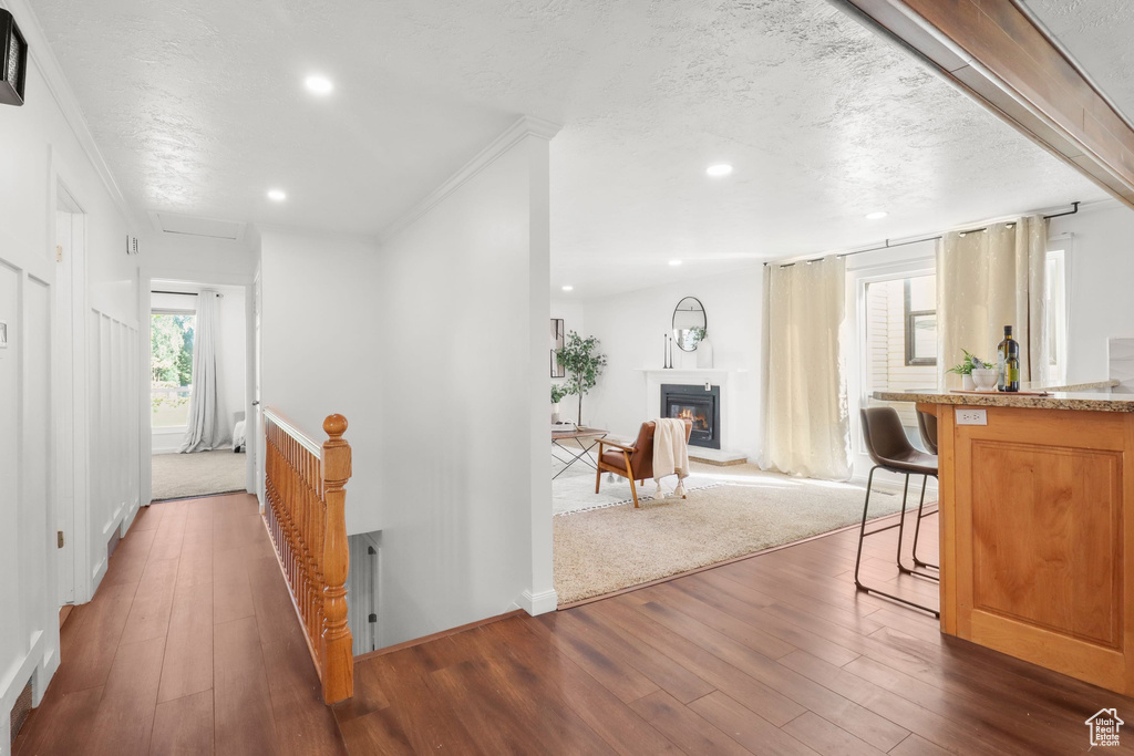 Hall featuring dark wood-style flooring, crown molding, a textured ceiling, an upstairs landing, and recessed lighting