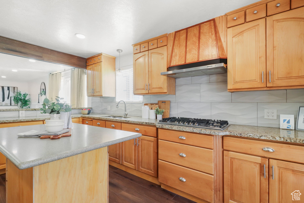 Kitchen with stainless steel gas stovetop, dark wood-style floors, under cabinet range hood, backsplash, and a kitchen island