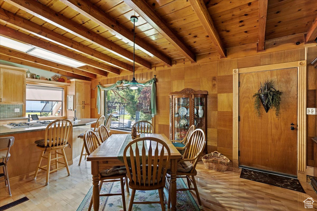Dining area featuring a wood ceiling with exposed beams, wooden walls, and light wood finished floors