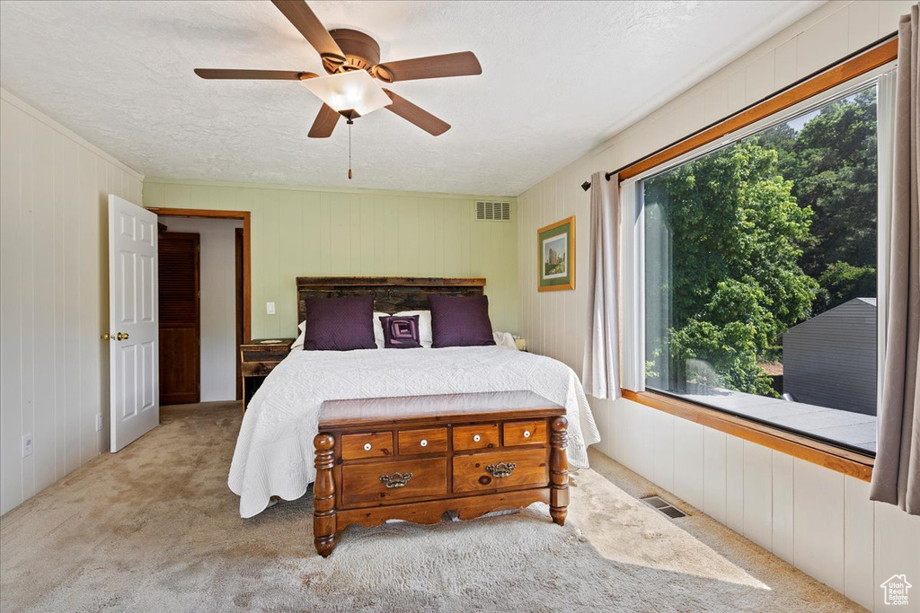 Bedroom with carpet floors, wood walls, a textured ceiling, and a ceiling fan