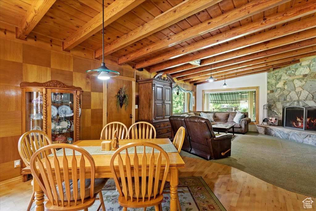 Dining room with a wood ceiling with exposed beams, wood walls, wood finished floors, and a fireplace
