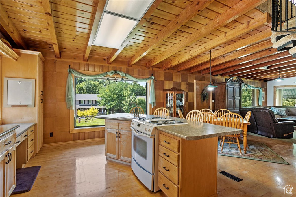 Kitchen with white range with gas cooktop, light wood-type flooring, wooden walls, a center island, and open floor plan