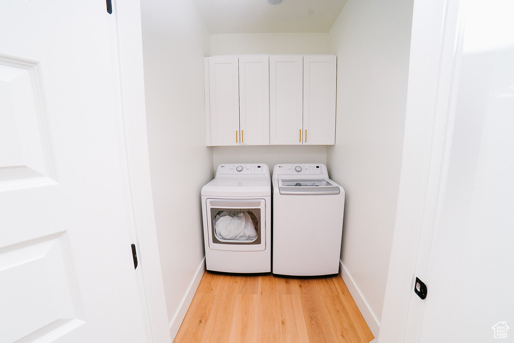 Washroom with washing machine and clothes dryer, light wood-style flooring, and cabinet space