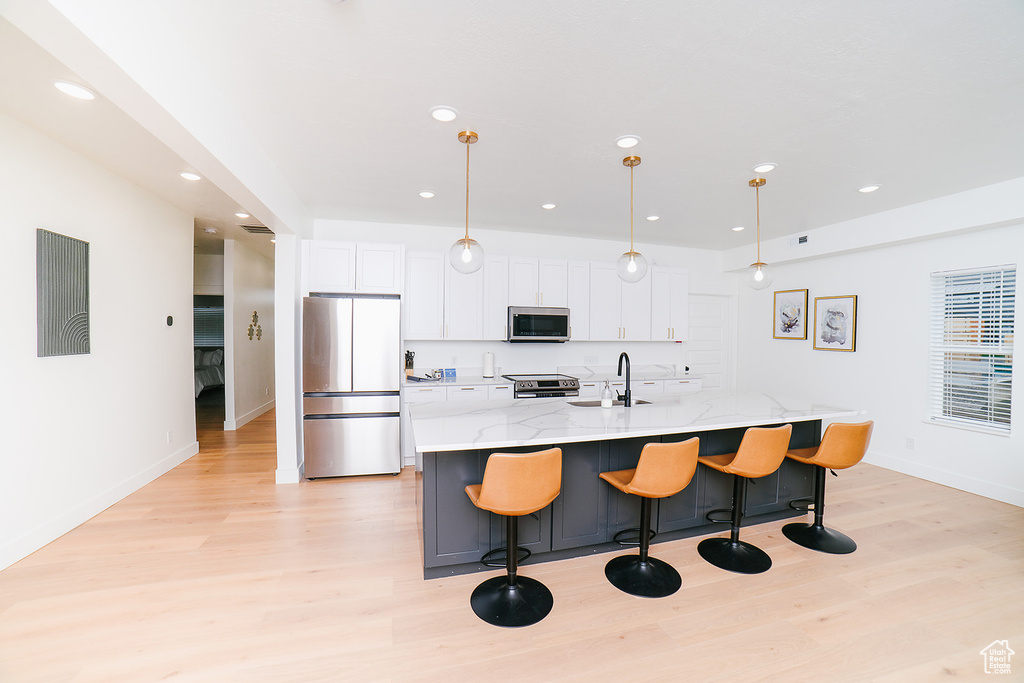 Kitchen with appliances with stainless steel finishes, light wood-style flooring, white cabinets, a center island with sink, and recessed lighting