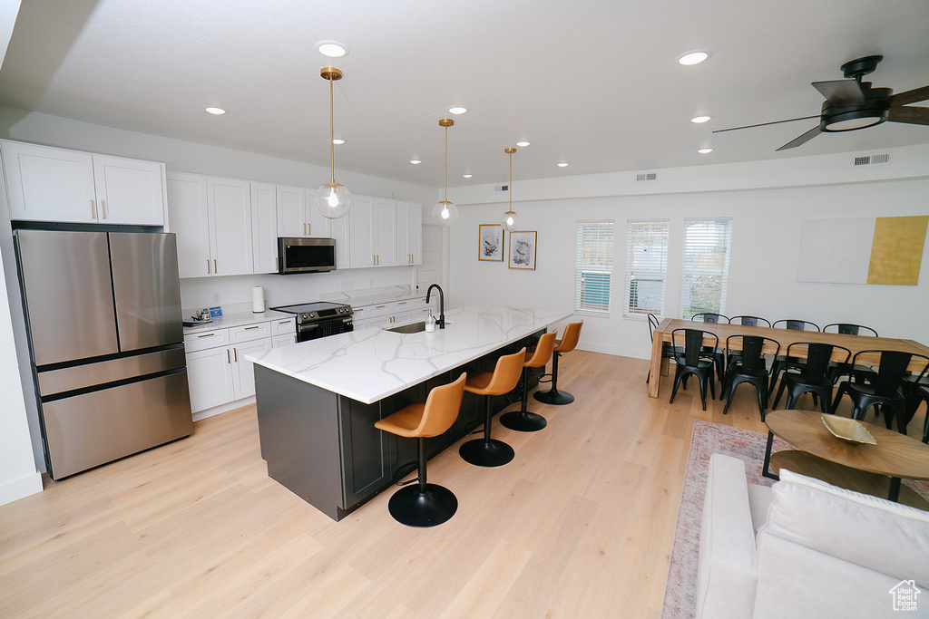 Kitchen featuring appliances with stainless steel finishes, light wood-type flooring, white cabinetry, a kitchen breakfast bar, and ceiling fan