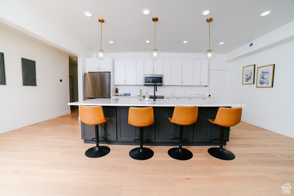 Kitchen with appliances with stainless steel finishes, a center island with sink, light wood-type flooring, white cabinetry, and recessed lighting