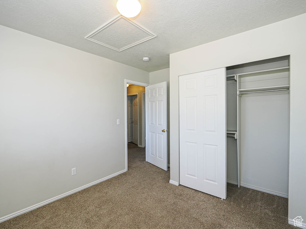 Unfurnished bedroom with attic access, carpet flooring, a textured ceiling, and a closet