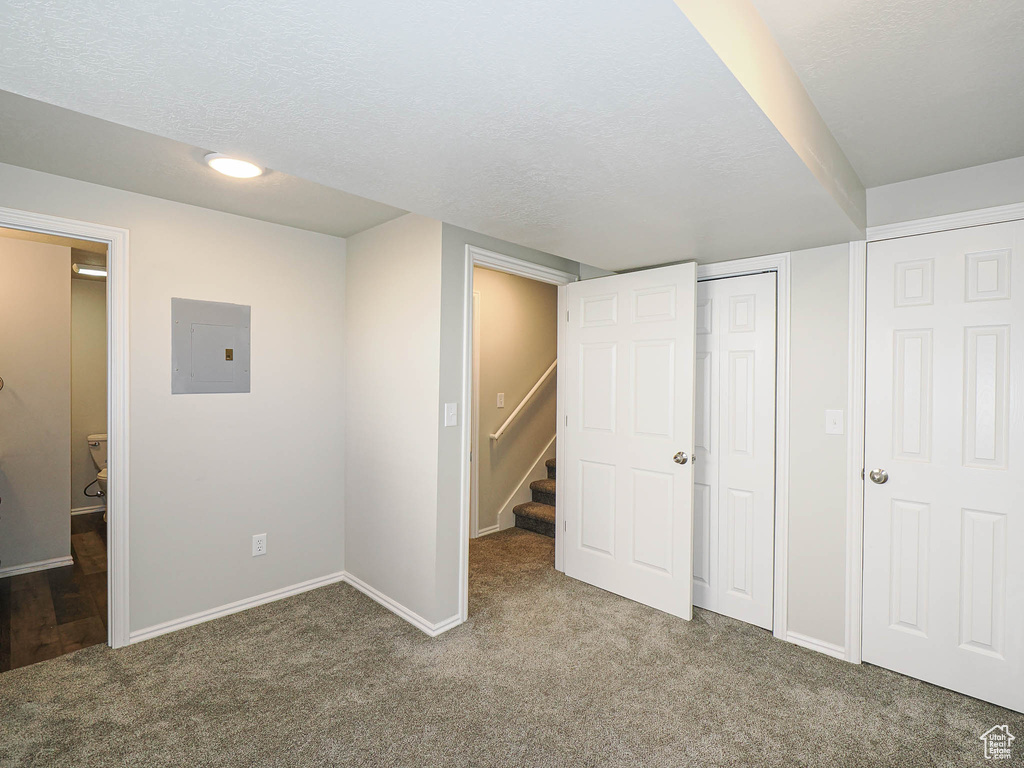 Finished below grade area with electric panel, carpet floors, stairs, and a textured ceiling