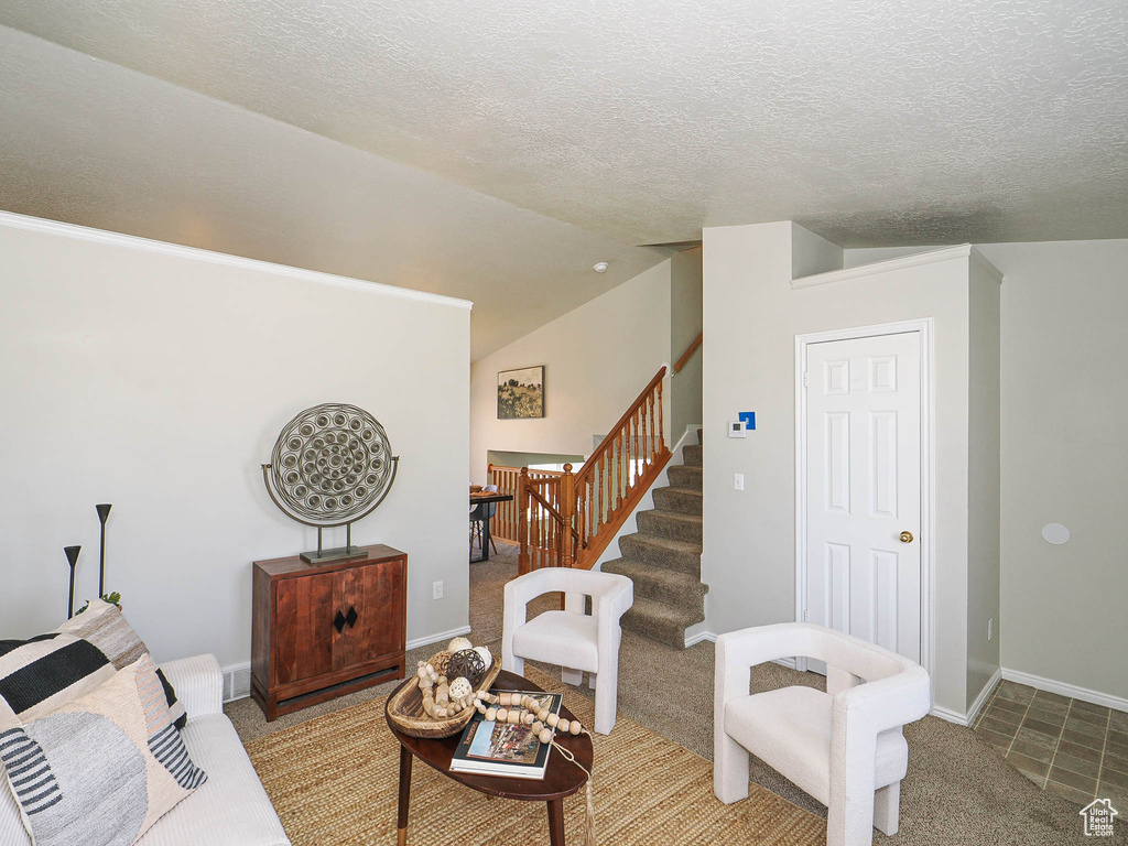 Living room featuring stairway, carpet, vaulted ceiling, and a textured ceiling
