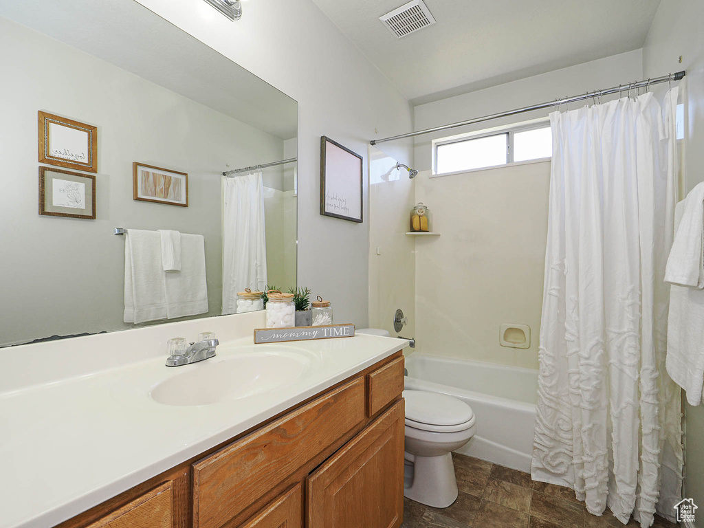 Full bath featuring vanity, shower / tub combo with curtain, and stone finish floors
