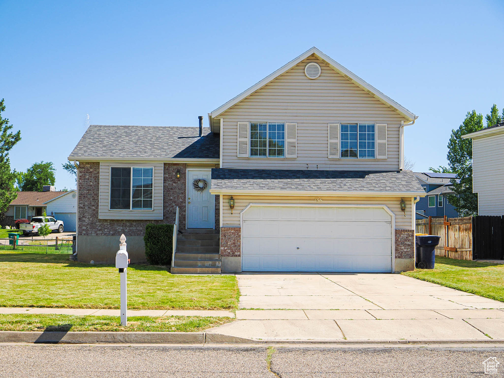 Split level home with an attached garage, brick siding, driveway, and a shingled roof
