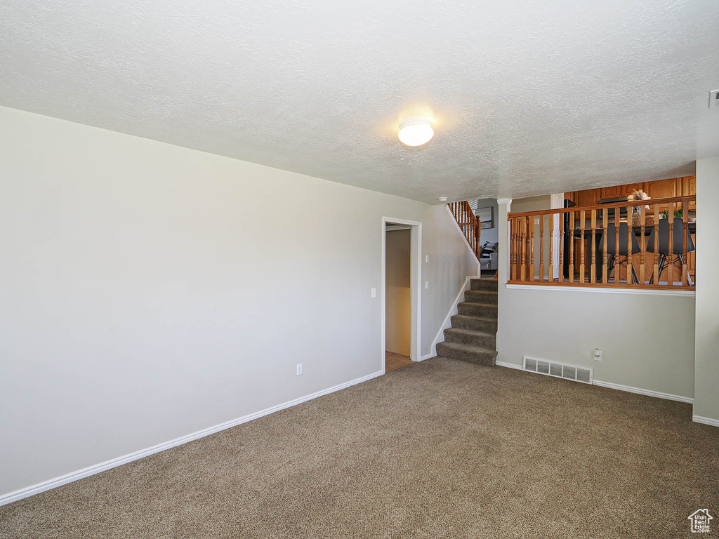Empty room with a textured ceiling, stairway, and carpet flooring