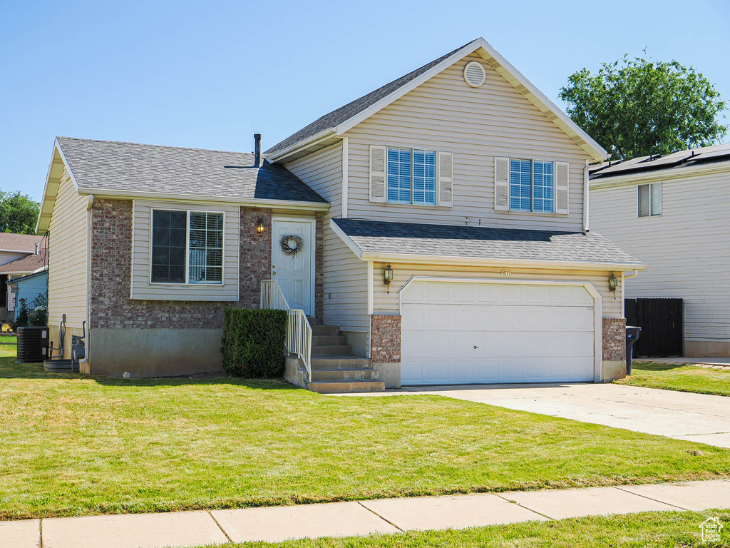 Split level home with an attached garage, driveway, a front yard, and brick siding