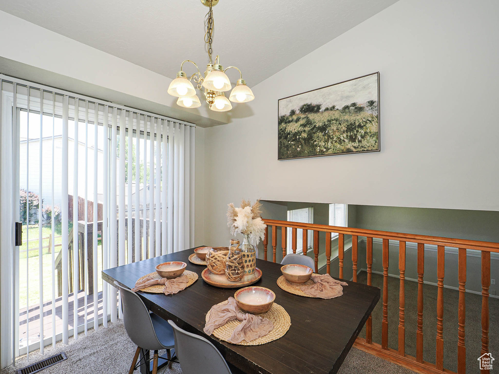 Carpeted dining room with vaulted ceiling and a chandelier