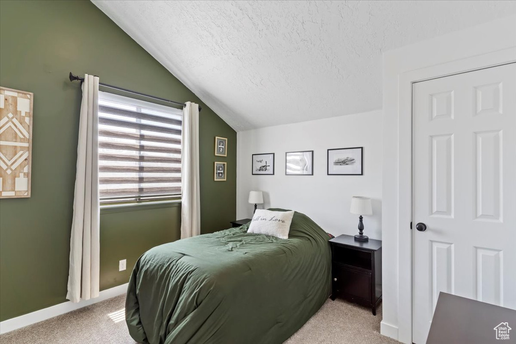 Carpeted bedroom featuring vaulted ceiling and a textured ceiling