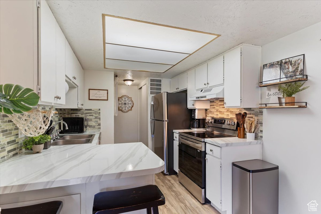 Kitchen with appliances with stainless steel finishes, under cabinet range hood, backsplash, light wood finished floors, and white cabinets