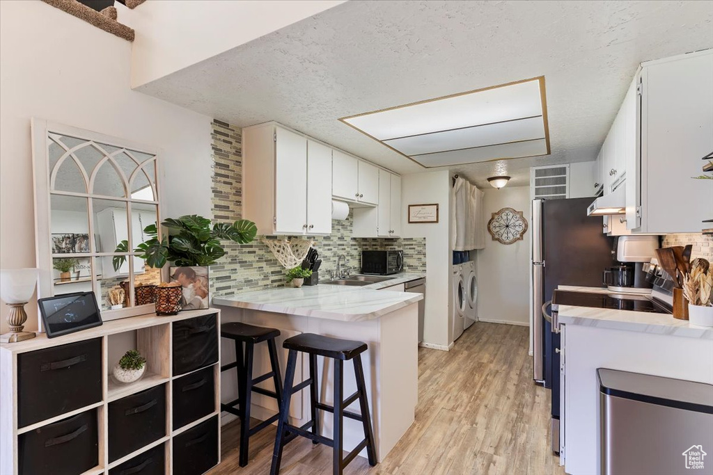 Kitchen with washer and dryer, black microwave, light countertops, a peninsula, and decorative backsplash