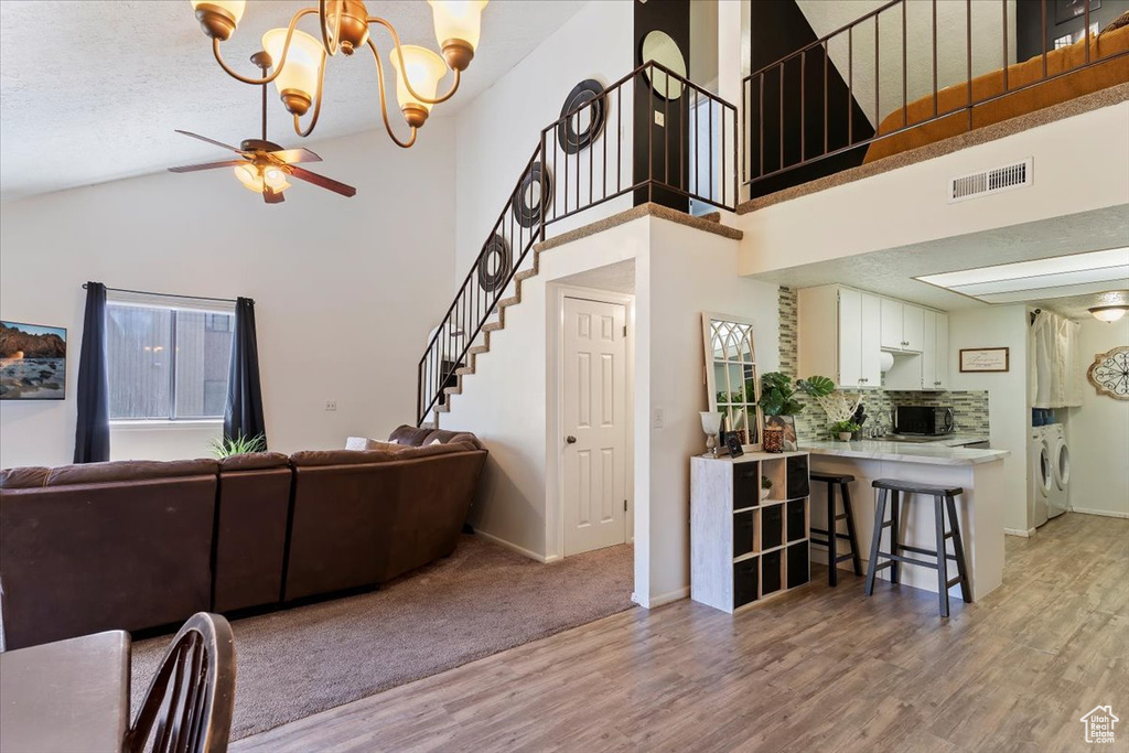Living room featuring washer and dryer, light wood-style floors, a chandelier, a ceiling fan, and stairway