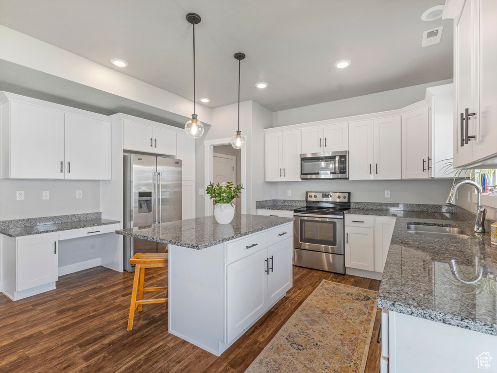 Kitchen featuring appliances with stainless steel finishes, dark wood-type flooring, a kitchen island, white cabinets, and recessed lighting
