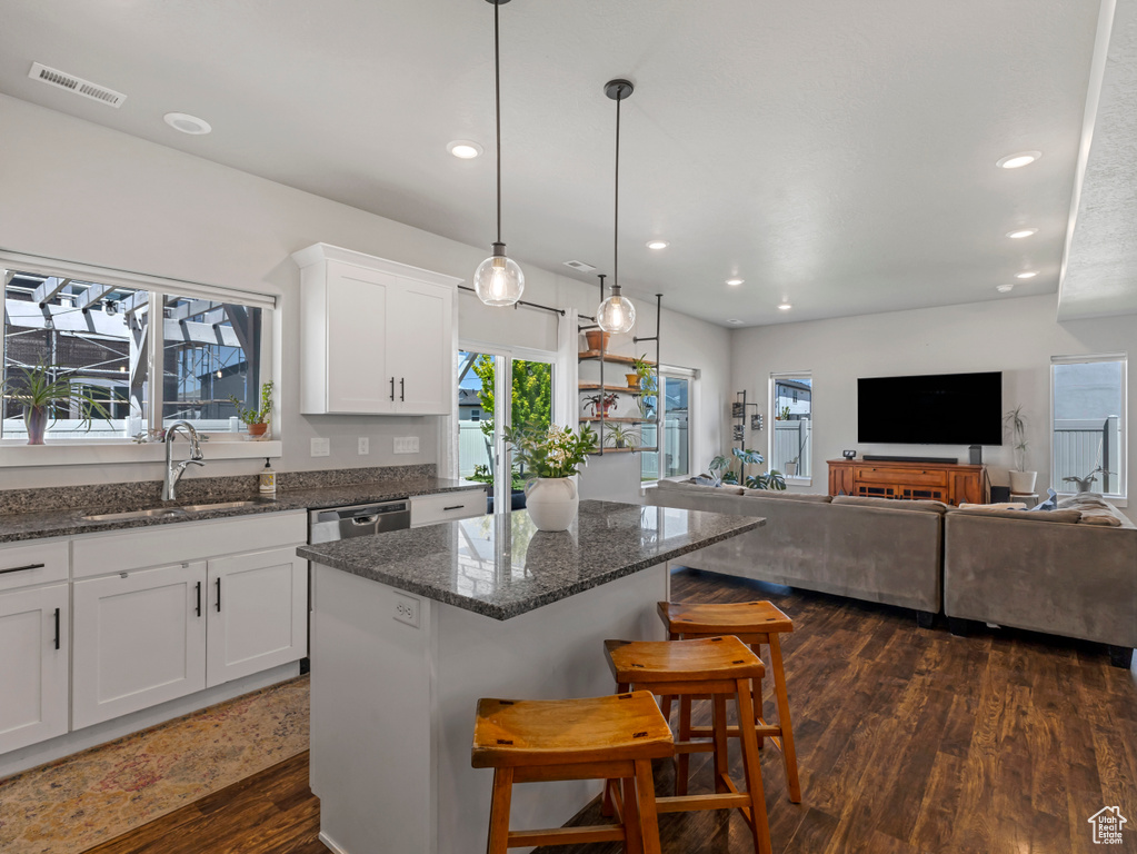 Kitchen featuring a kitchen island, white cabinets, recessed lighting, a kitchen bar, and dark stone countertops