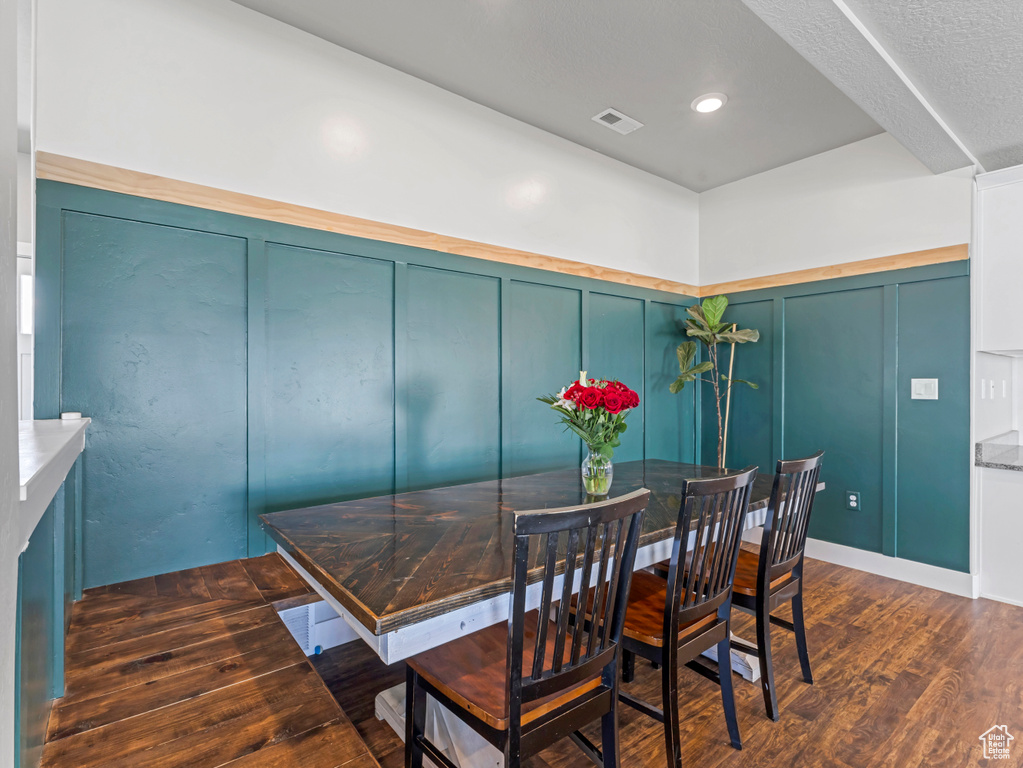 Dining space featuring a decorative wall, dark wood finished floors, and wainscoting