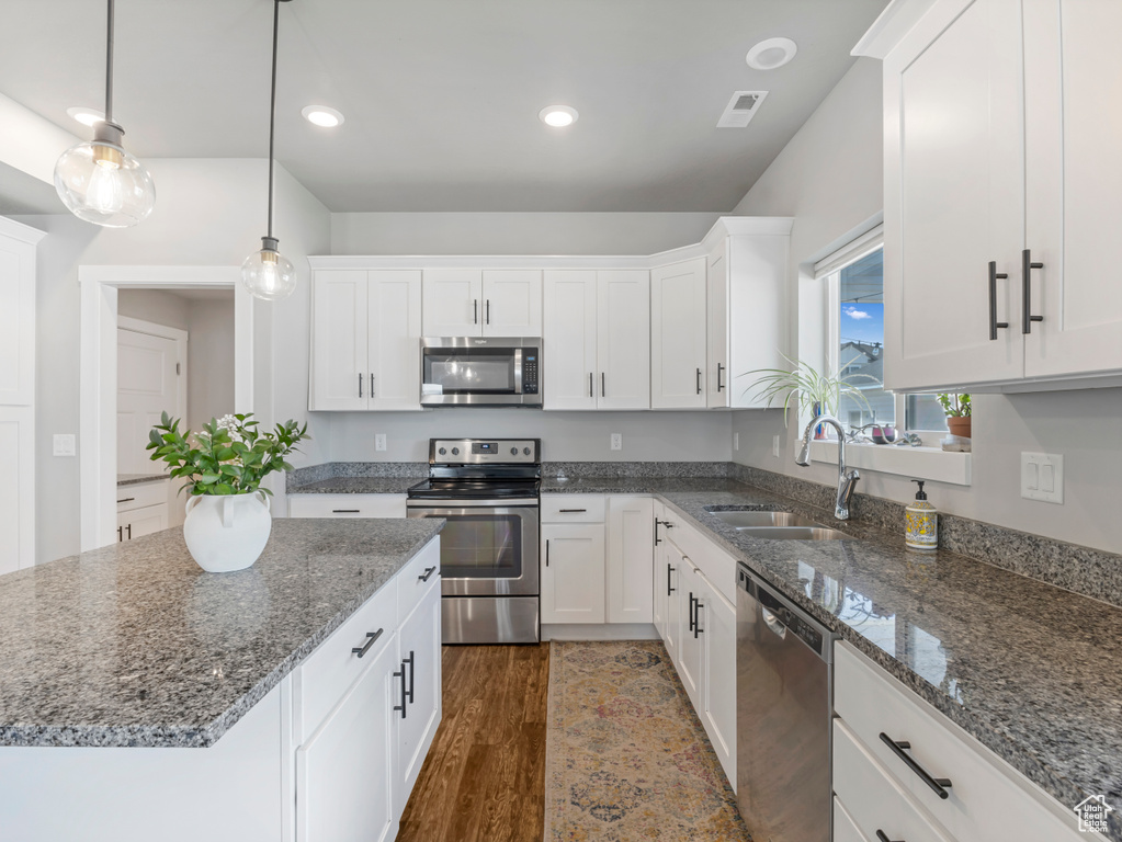 Kitchen featuring appliances with stainless steel finishes, white cabinets, dark wood-type flooring, stone countertops, and recessed lighting