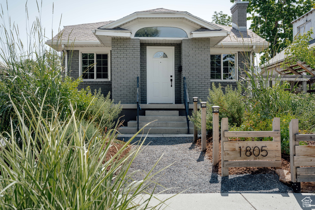 View of front of home featuring brick siding, a chimney, and entry steps