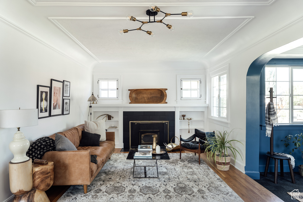 Living room with arched walkways, plenty of natural light, wood finished floors, ornamental molding, and a fireplace with flush hearth