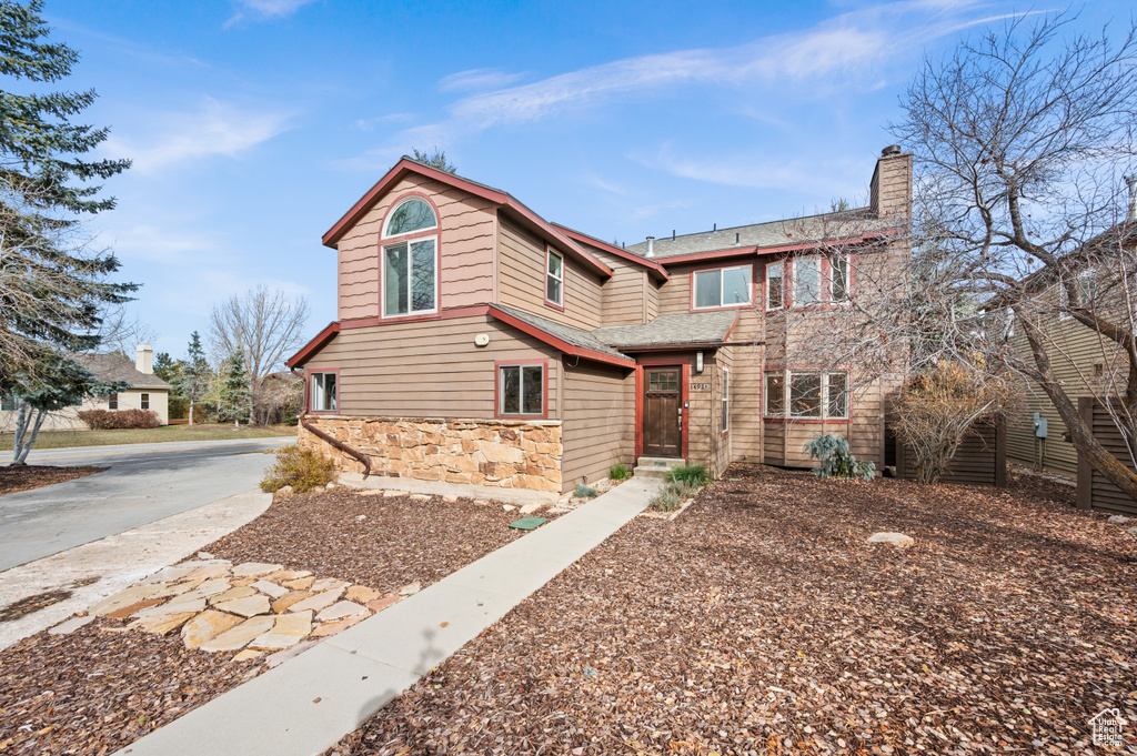 View of front of home featuring stone siding, a chimney, and a shingled roof