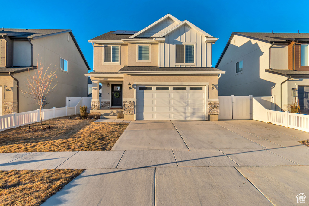 View of front facade with an attached garage, solar panels, concrete driveway, and stone siding