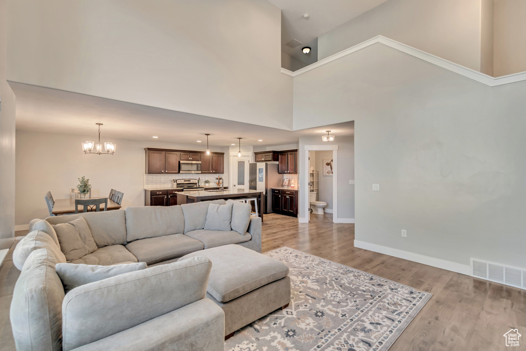 Living area featuring a chandelier, light wood-style flooring, a high ceiling, and recessed lighting
