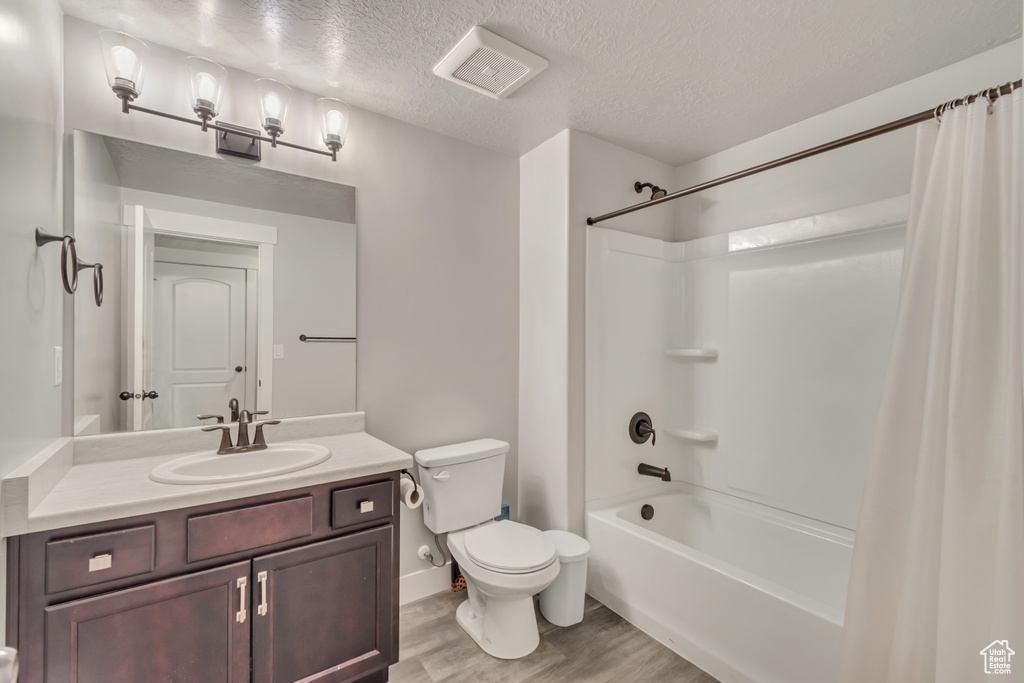 Bathroom featuring wood finished floors, shower / bath combination with curtain, vanity, and a textured ceiling