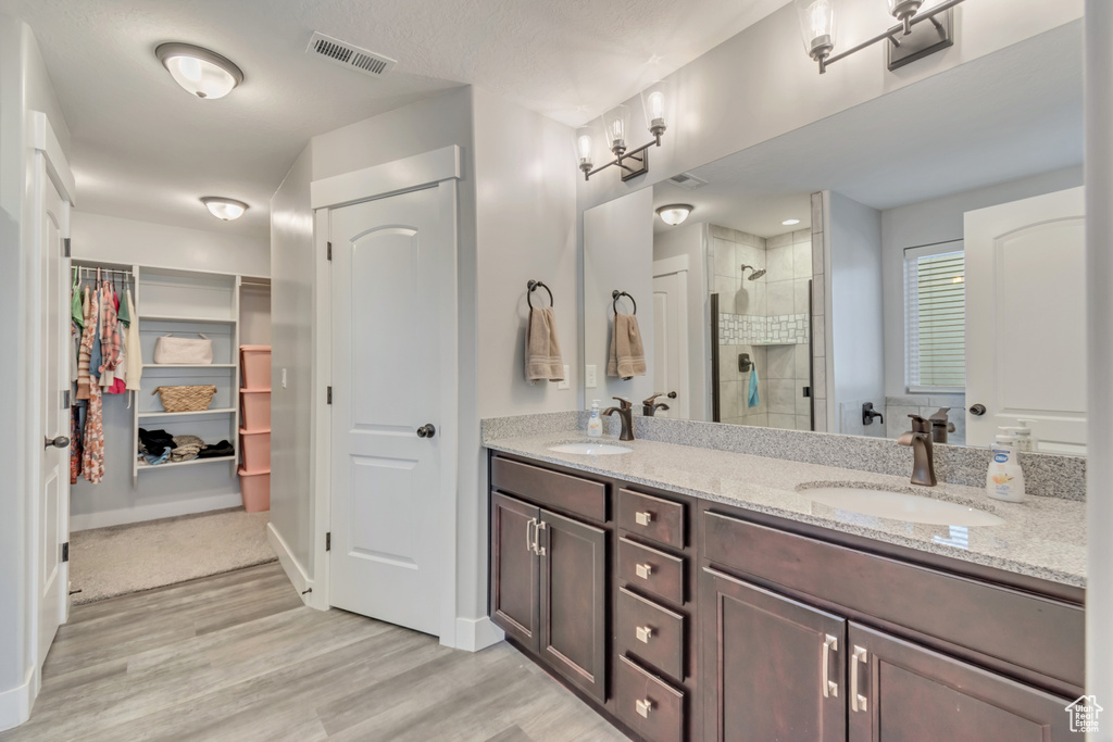 Bathroom with double vanity, a shower stall, a walk in closet, and wood finished floors
