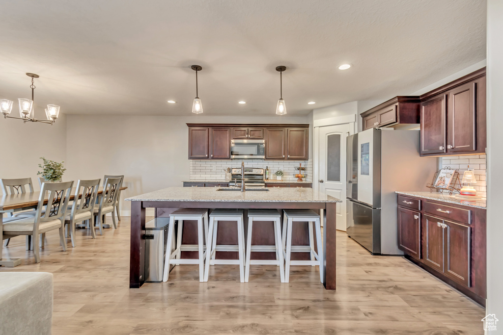 Kitchen featuring stainless steel appliances, decorative backsplash, a breakfast bar, decorative light fixtures, and recessed lighting