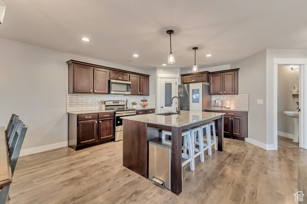 Kitchen with appliances with stainless steel finishes, decorative backsplash, light wood finished floors, a breakfast bar, and dark brown cabinets