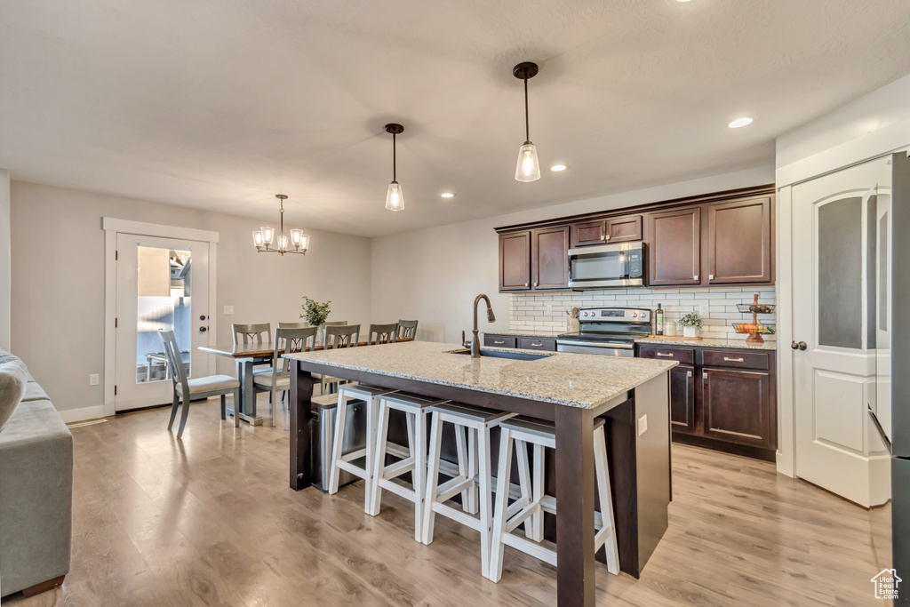 Kitchen featuring stainless steel appliances, dark brown cabinetry, a breakfast bar, decorative backsplash, and light wood-style flooring