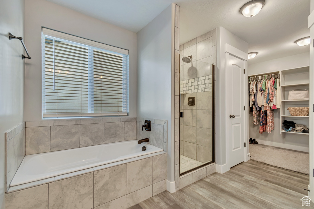 Full bath with a garden tub, a stall shower, a spacious closet, and wood finished floors