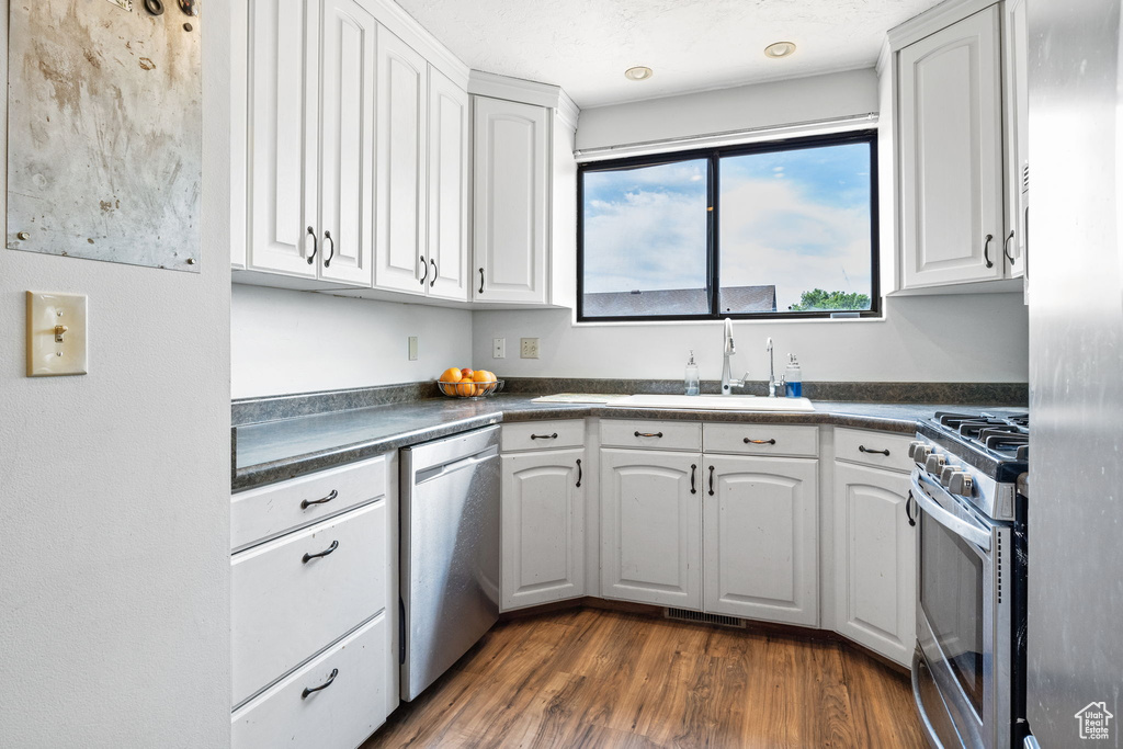 Kitchen with stainless steel appliances, dark countertops, white cabinetry, and dark wood-type flooring