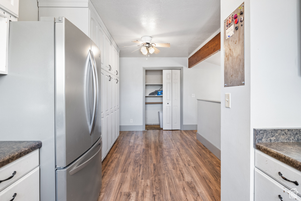 Kitchen featuring freestanding refrigerator, dark countertops, white cabinets, ceiling fan, and dark wood finished floors