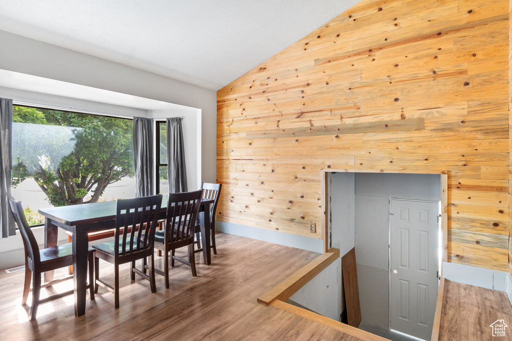 Dining area featuring vaulted ceiling, wooden walls, and wood finished floors