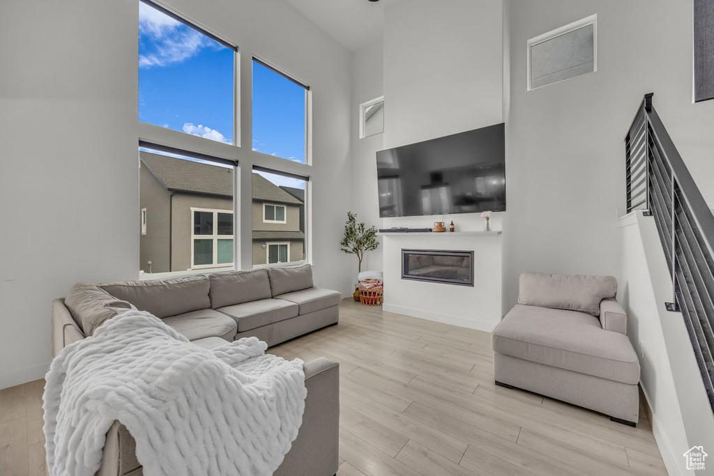 Living room with a high ceiling, a glass covered fireplace, and light wood-style flooring