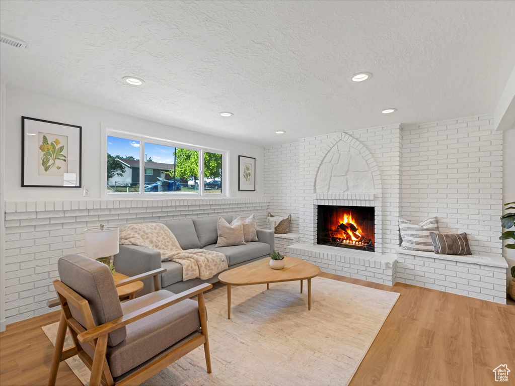Living room with a textured ceiling, a brick fireplace, wood finished floors, recessed lighting, and brick wall