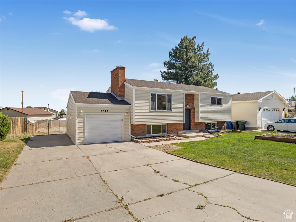 Raised ranch with a garage, concrete driveway, a chimney, and brick siding